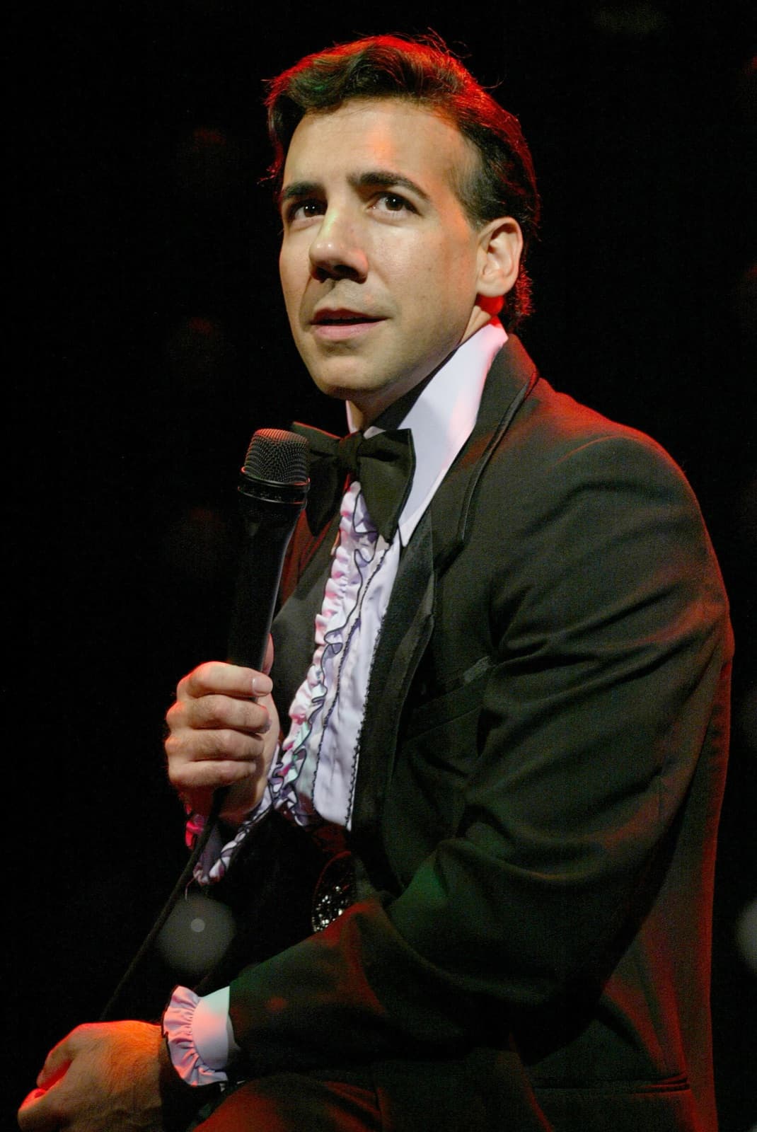 Chaz Esposito in a tuxedo with ruffled shirt, holding a microphone in character as Bobby Darin