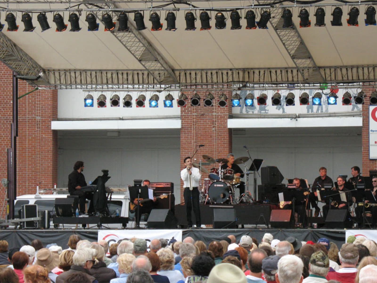 Wide view of a bandshell stage with the full band and a seated audience