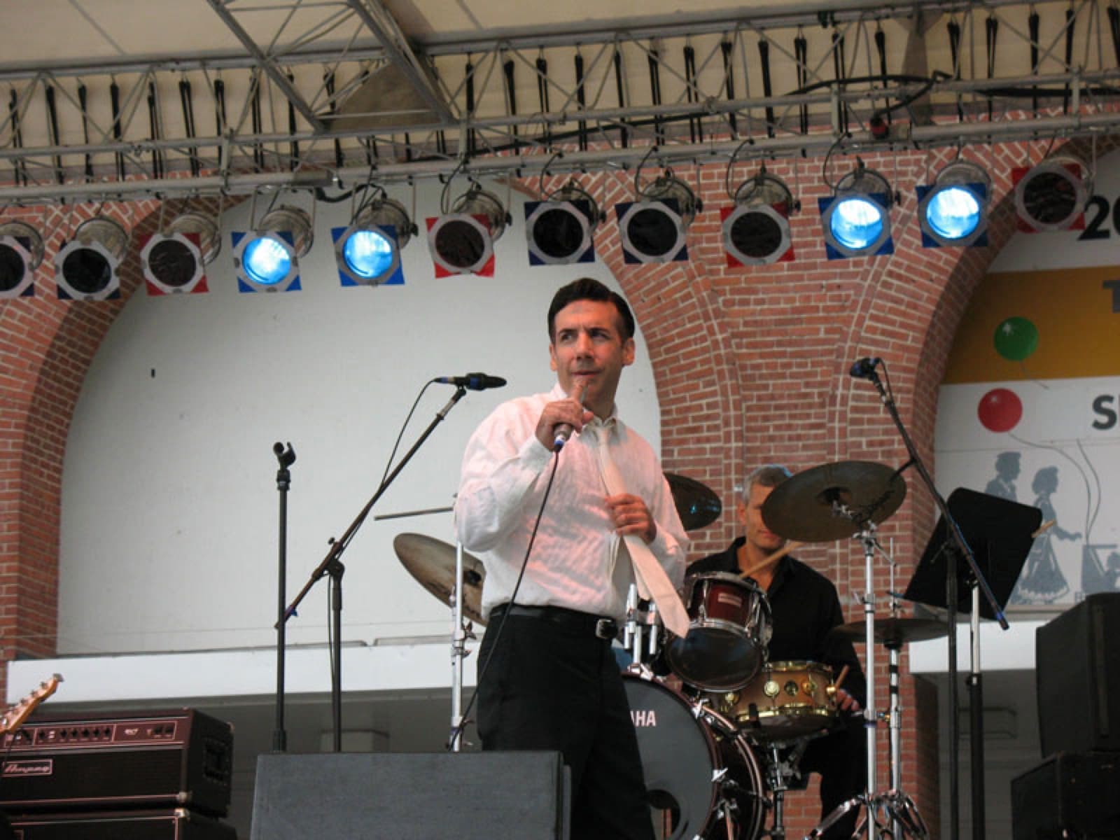 Chaz Esposito at the microphone on a fair stage, drum kit behind him