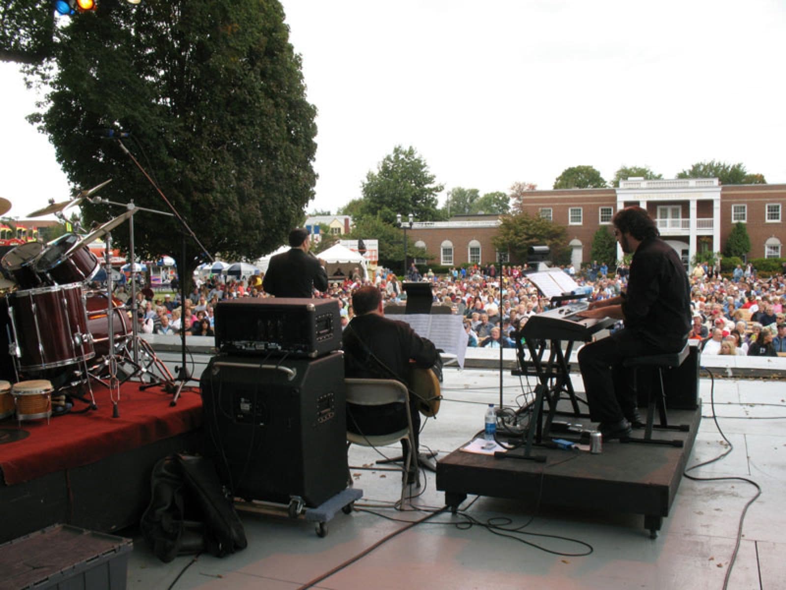 View from behind the band of a large outdoor festival crowd on a town green