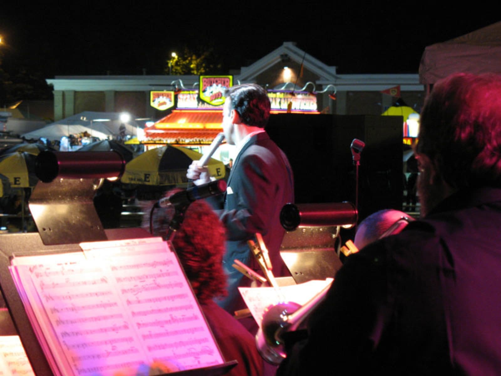 Night shot from the bandstand looking past music charts toward the fair midway lights