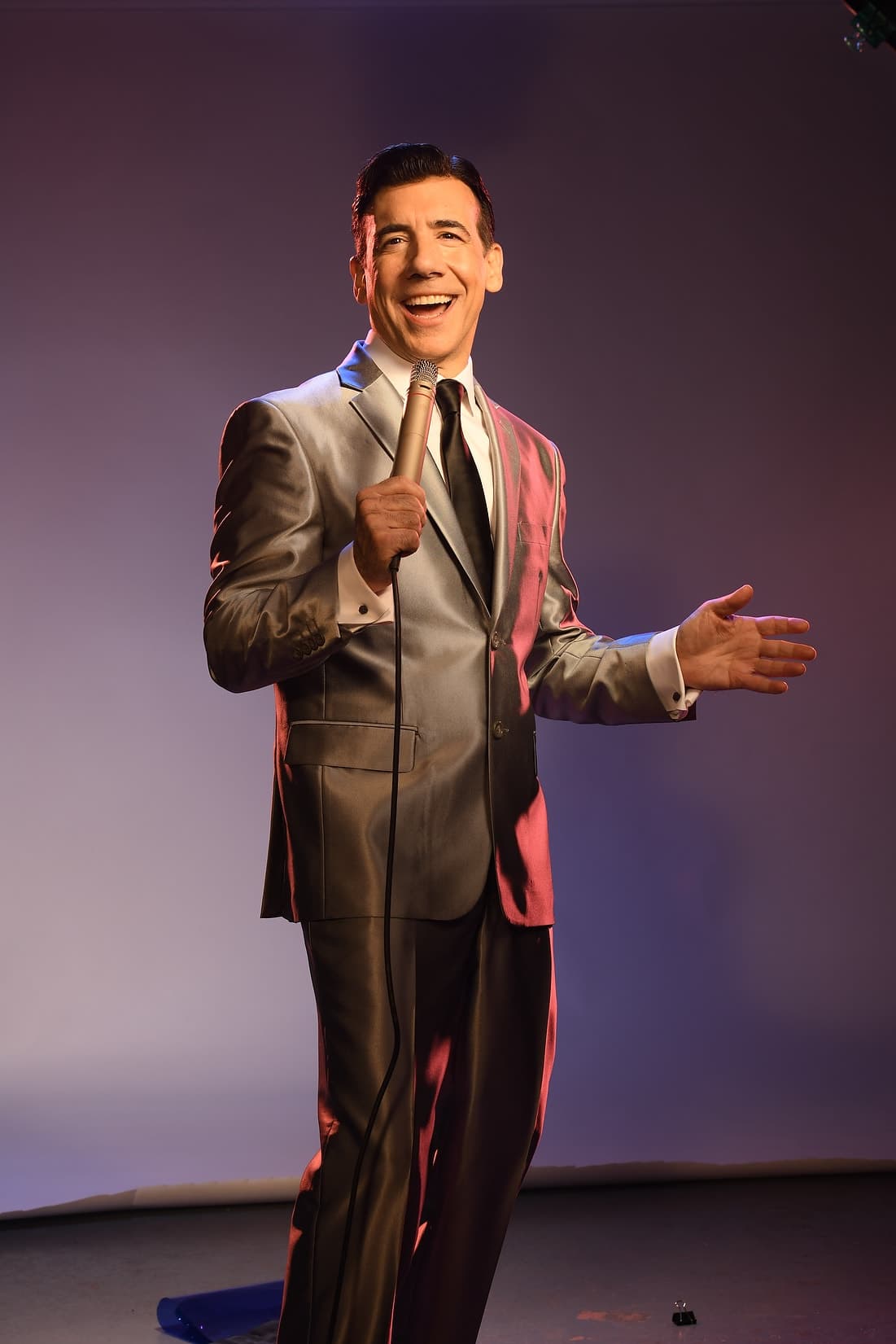Chaz Esposito smiling in a silver suit, microphone in hand