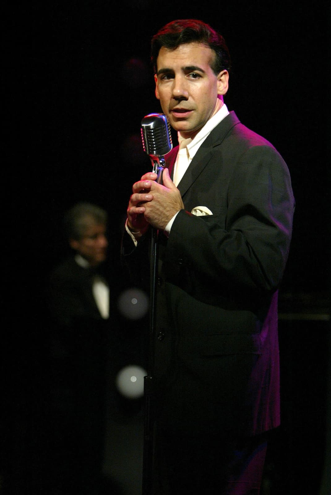 Chaz Esposito in a dark suit singing at a vintage chrome microphone